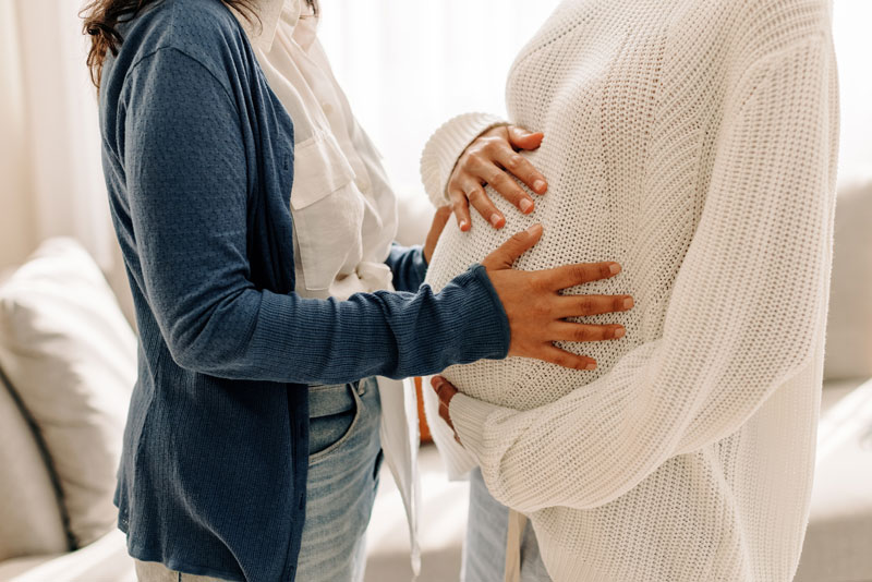 young-woman-touching-her-surrogate's-pregnant-belly A woman touching her surrogate's pregnant belly